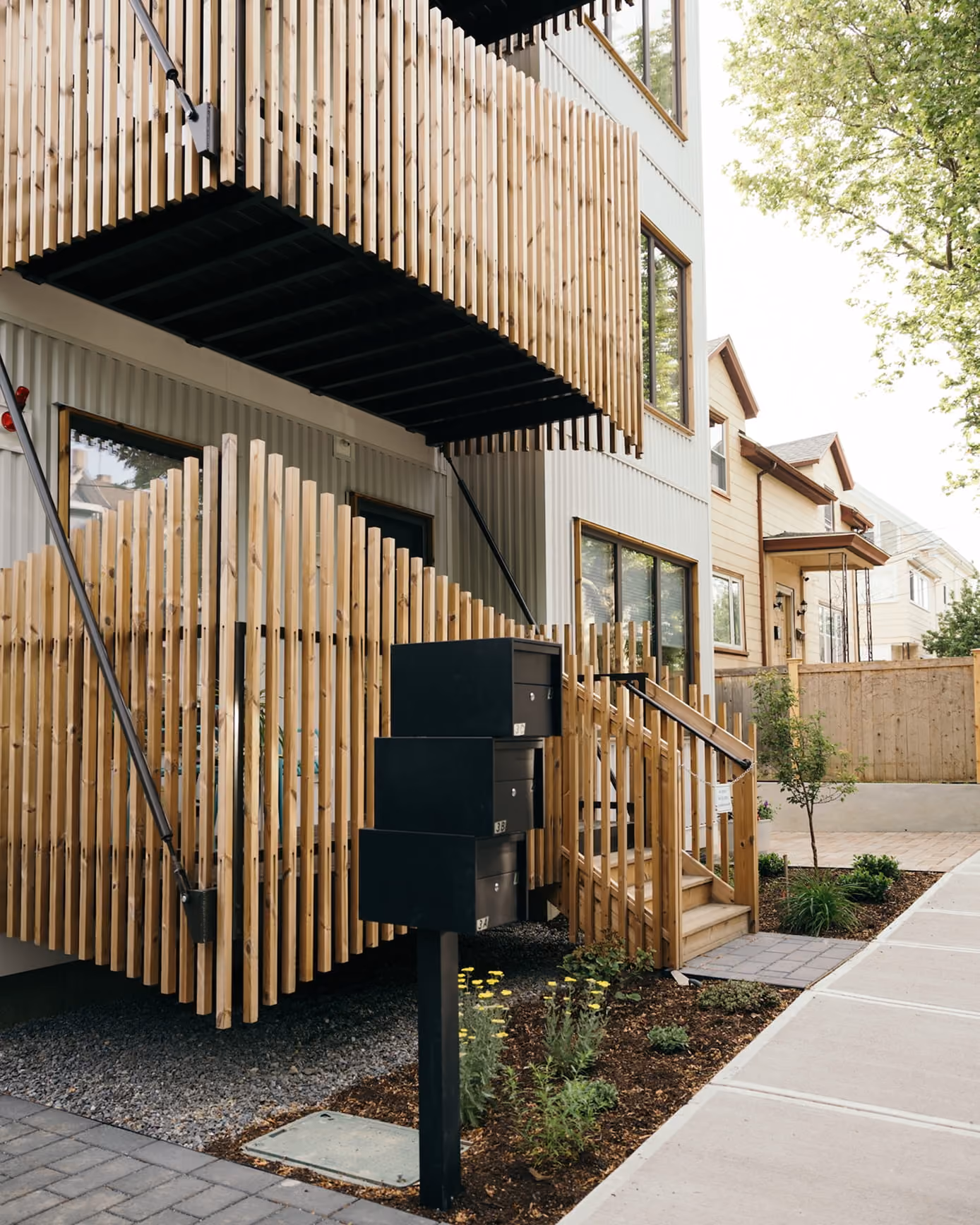 Side view of an Adams Circle townhouse with natural wood cladding, balconies, and a fenced patio.
