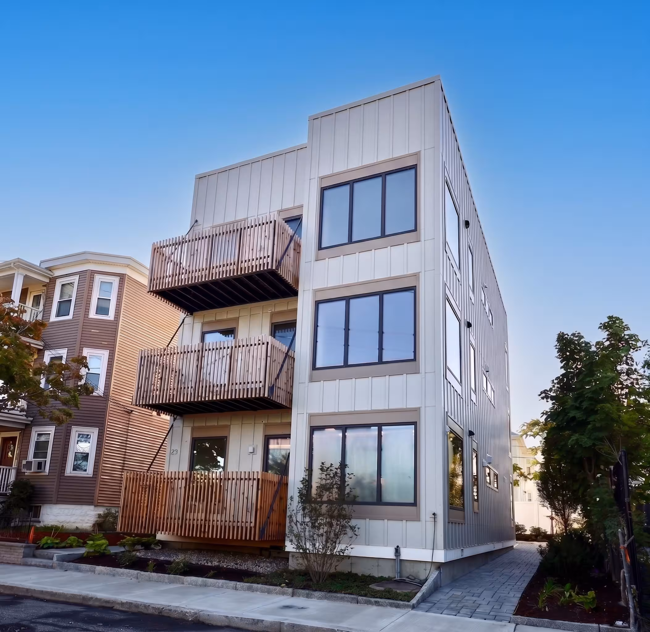 Street view of a modern multi-story residential building with large windows and wooden balconies.