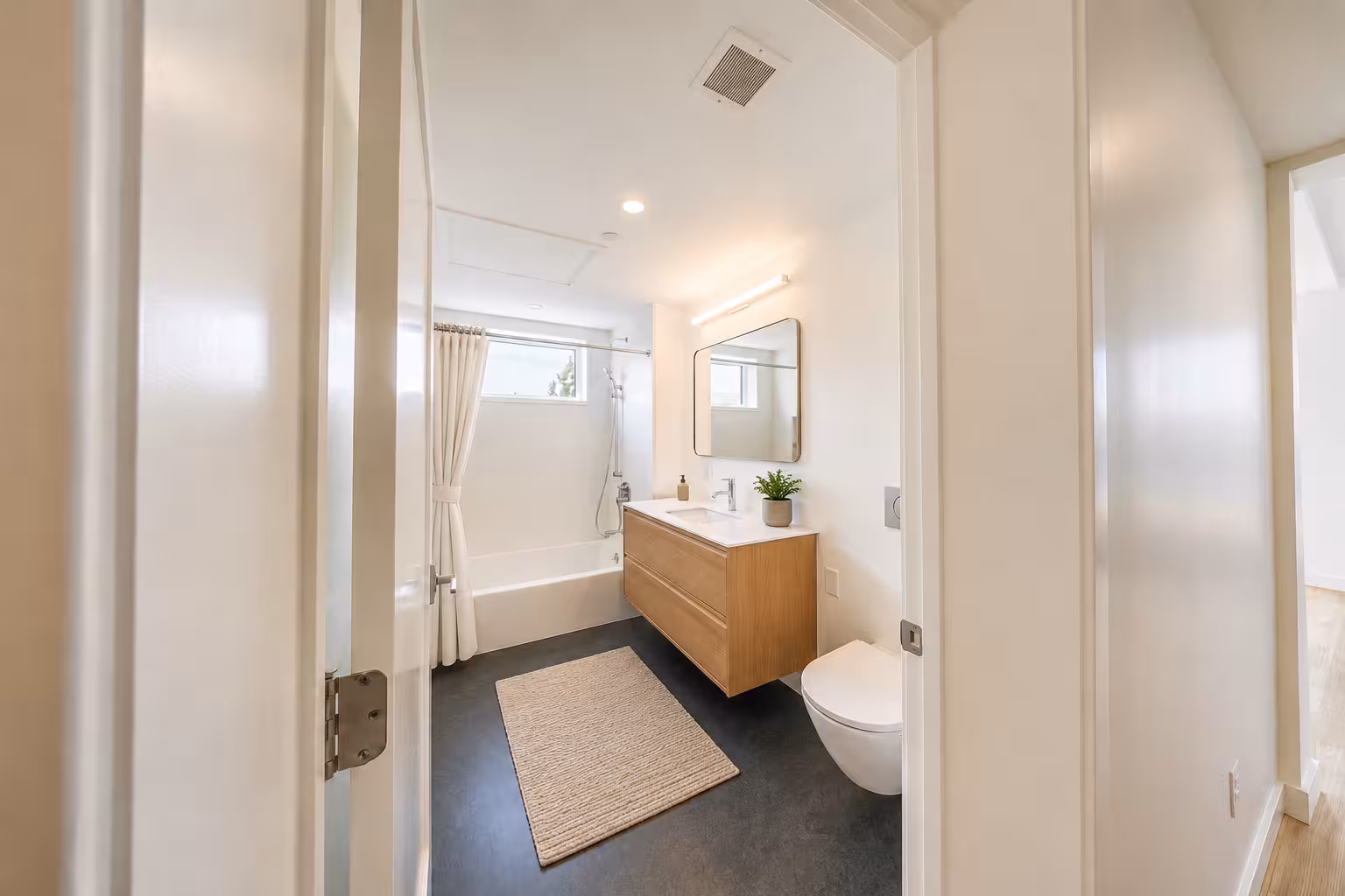 Compact modern bathroom with a white vanity, toilet, dark flooring, and light-colored walls.