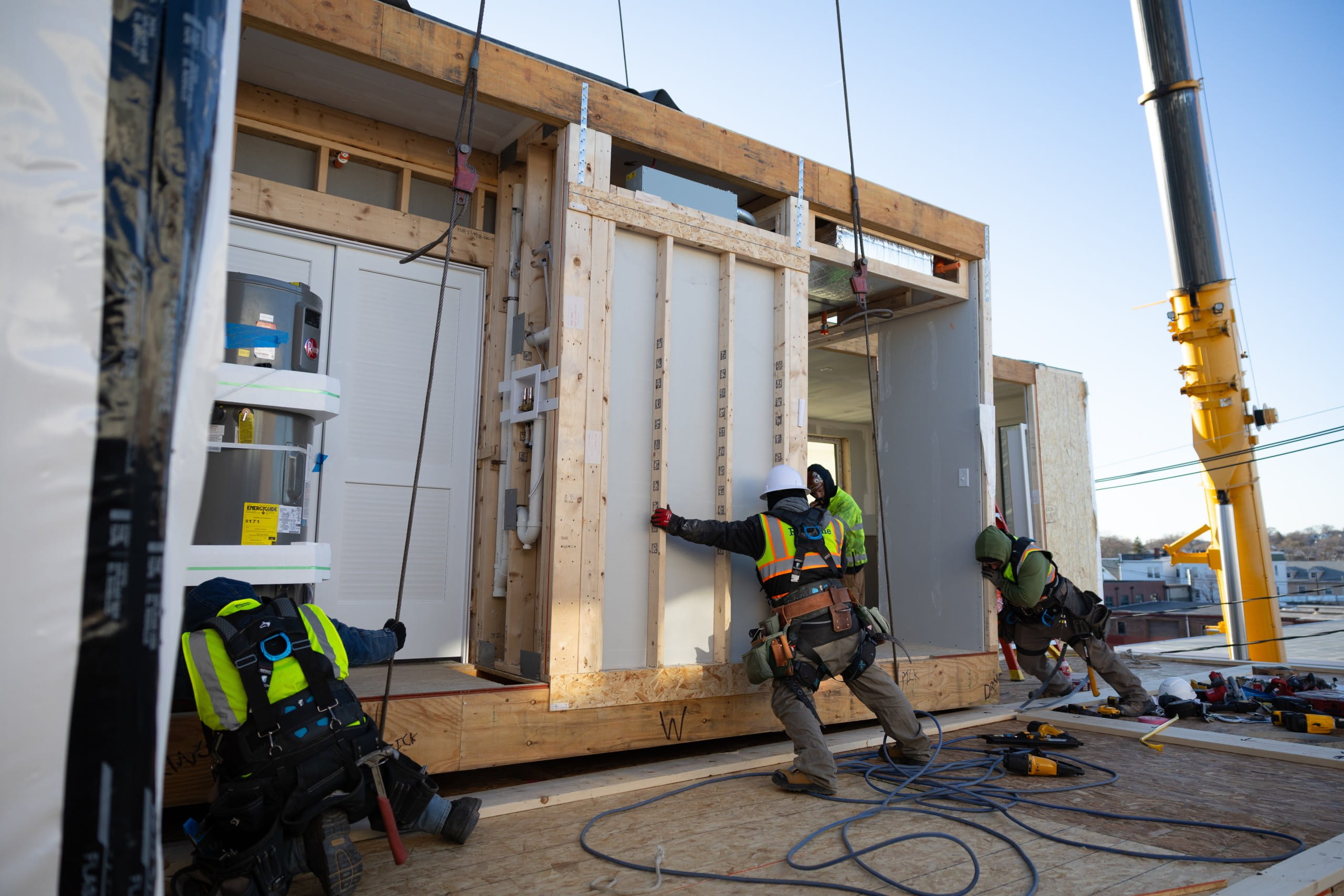 Construction crew working around large prefabricated wall panels while a crane operates at the site.