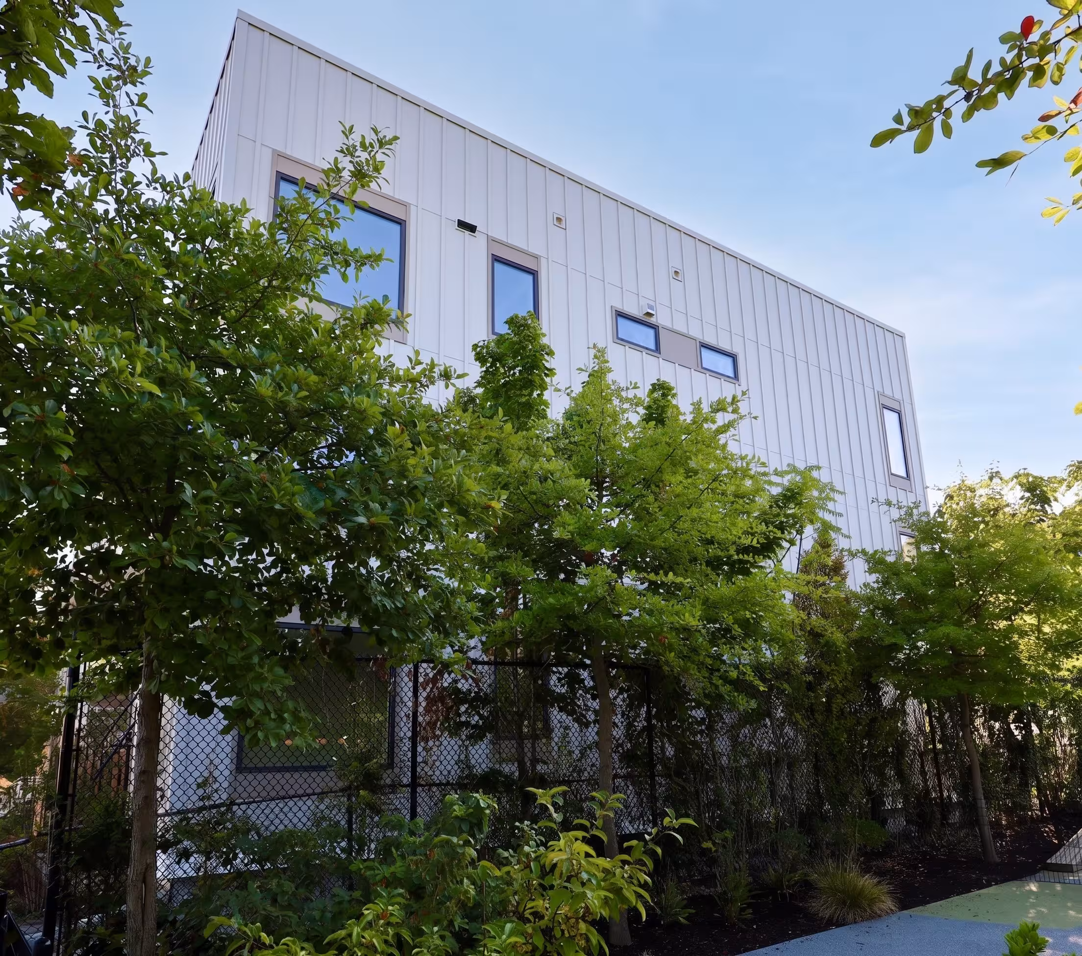 White multi-story residential building partially framed by leafy green trees.