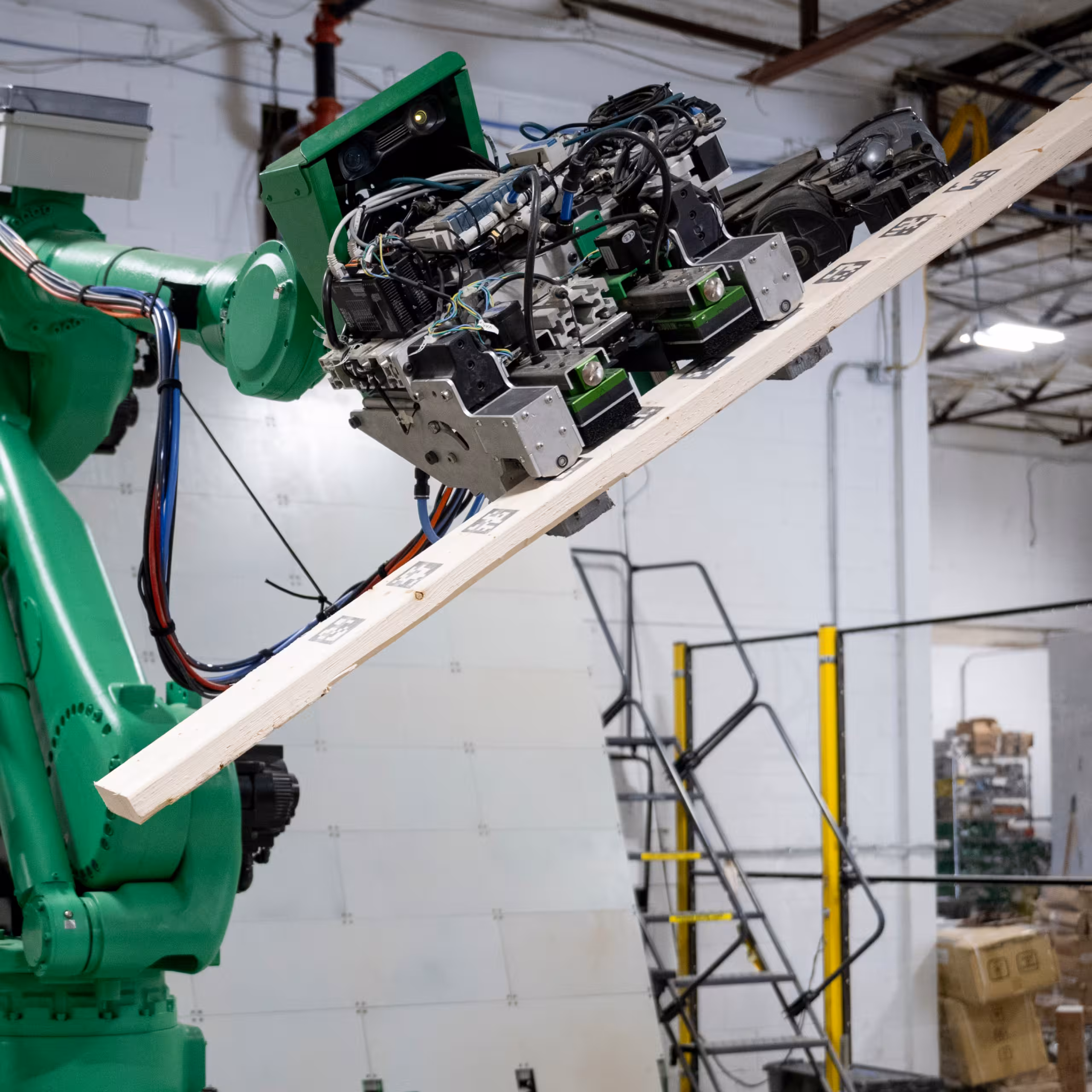 Green robotic arm inside the Reframe Systems microfactory lifting a length of lumber during fabrication.
