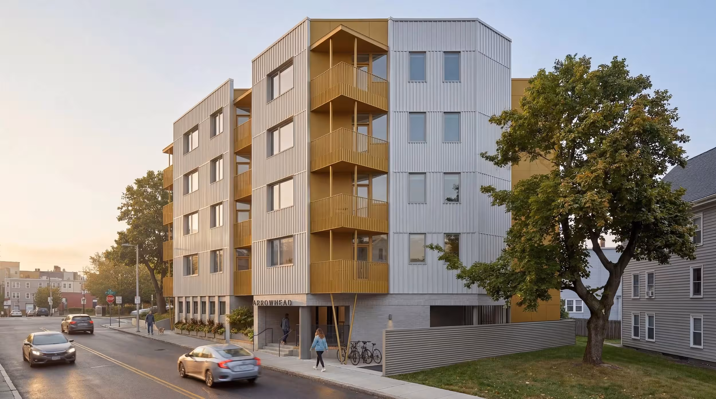 Corner exterior of a five-story modular apartment building in Roxbury, Boston, showing gold and gray metal cladding designed for Passive House performance.
