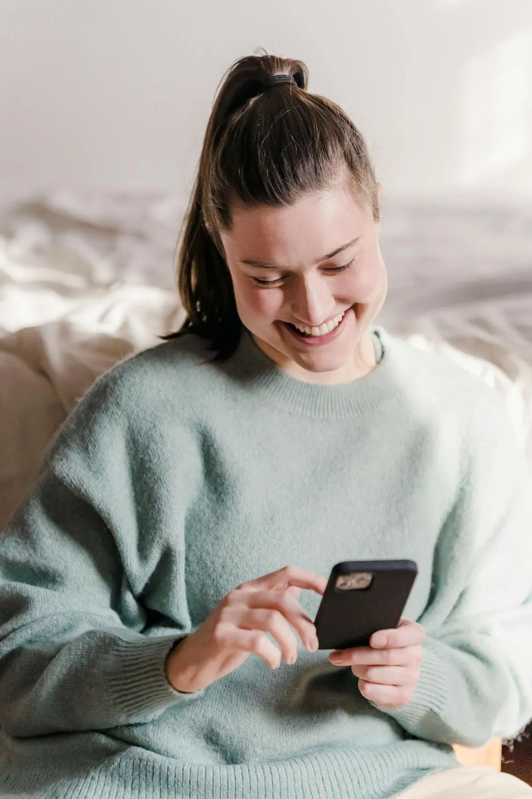 A woman sitting on a bed looking at a cell phone.