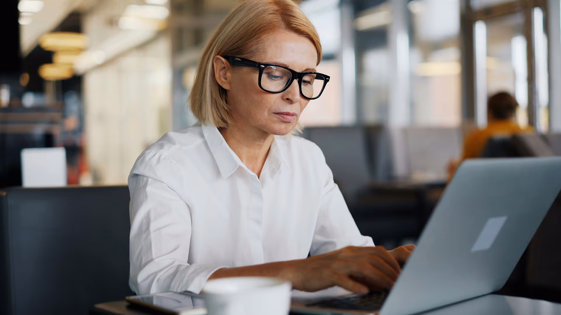 Professional woman working on laptop in modern office with coffee cup