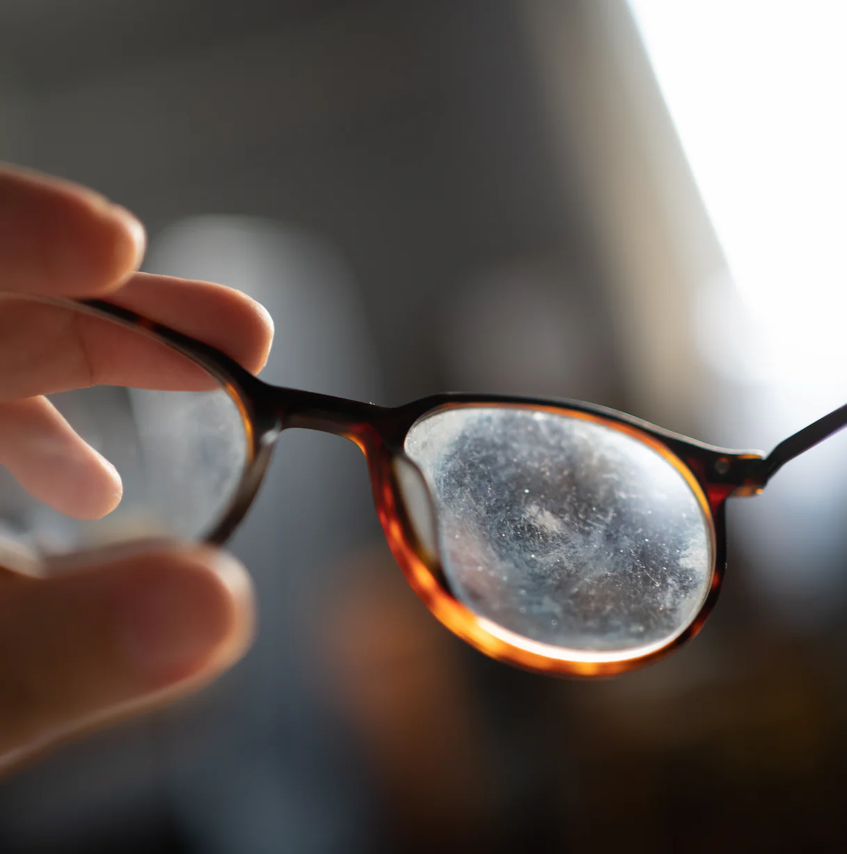 Tortoiseshell glasses with smudged lens held by a hand