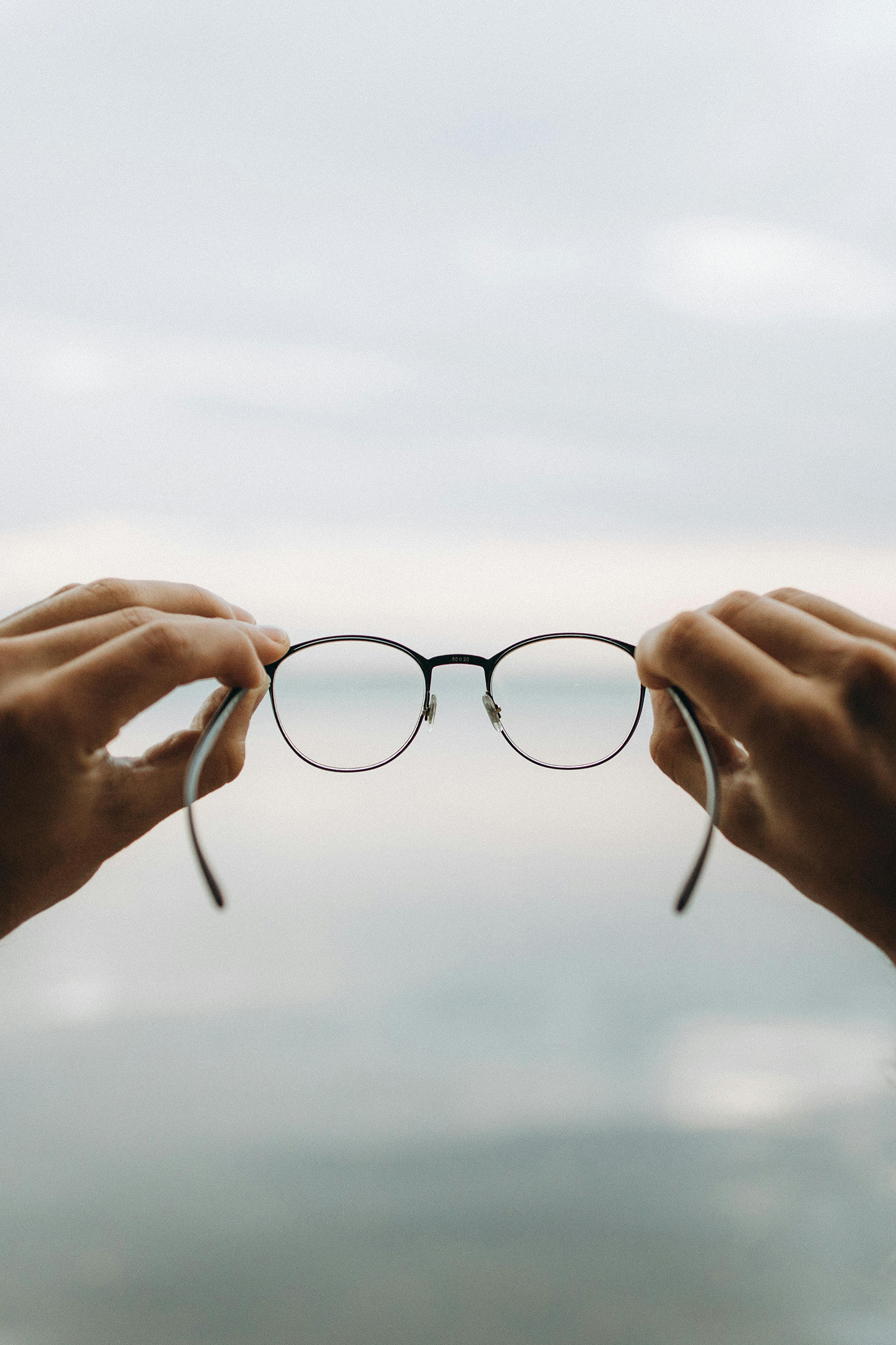 Hands holding round metal-framed eyeglasses against soft blue background