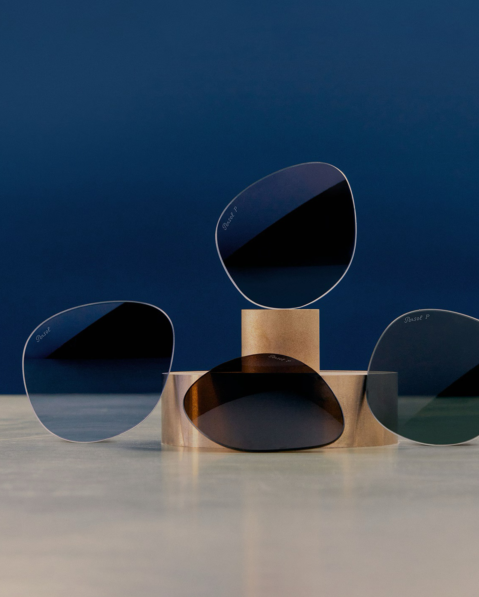 Polarized sunglasses lenses on minimalist gold pedestals against blue background