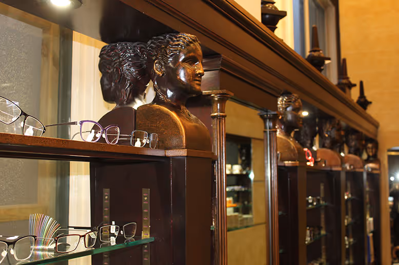 Bronze busts and eyeglasses displayed on wooden shelves in an elegant store
