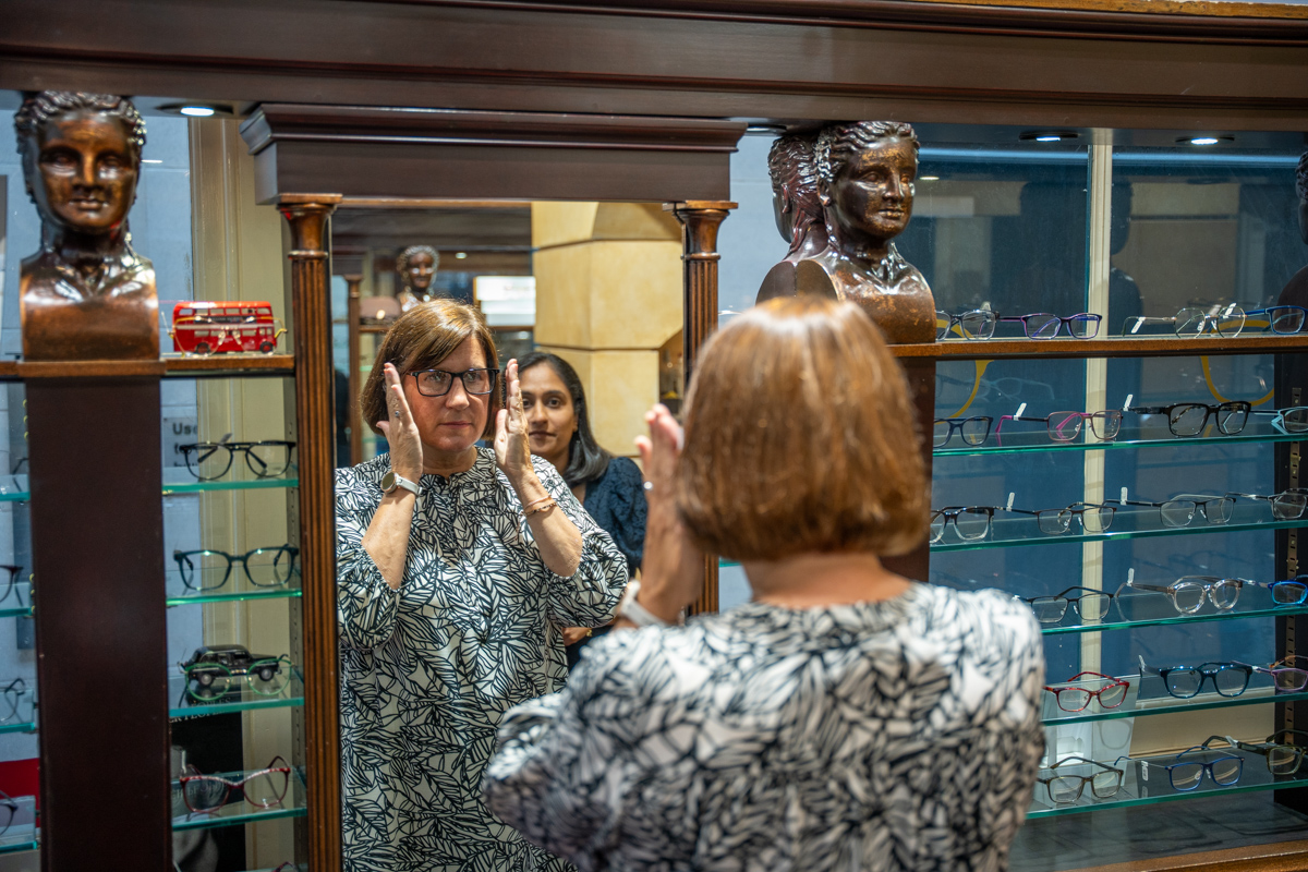 Woman trying on glasses in optical store with mirror and display shelves
