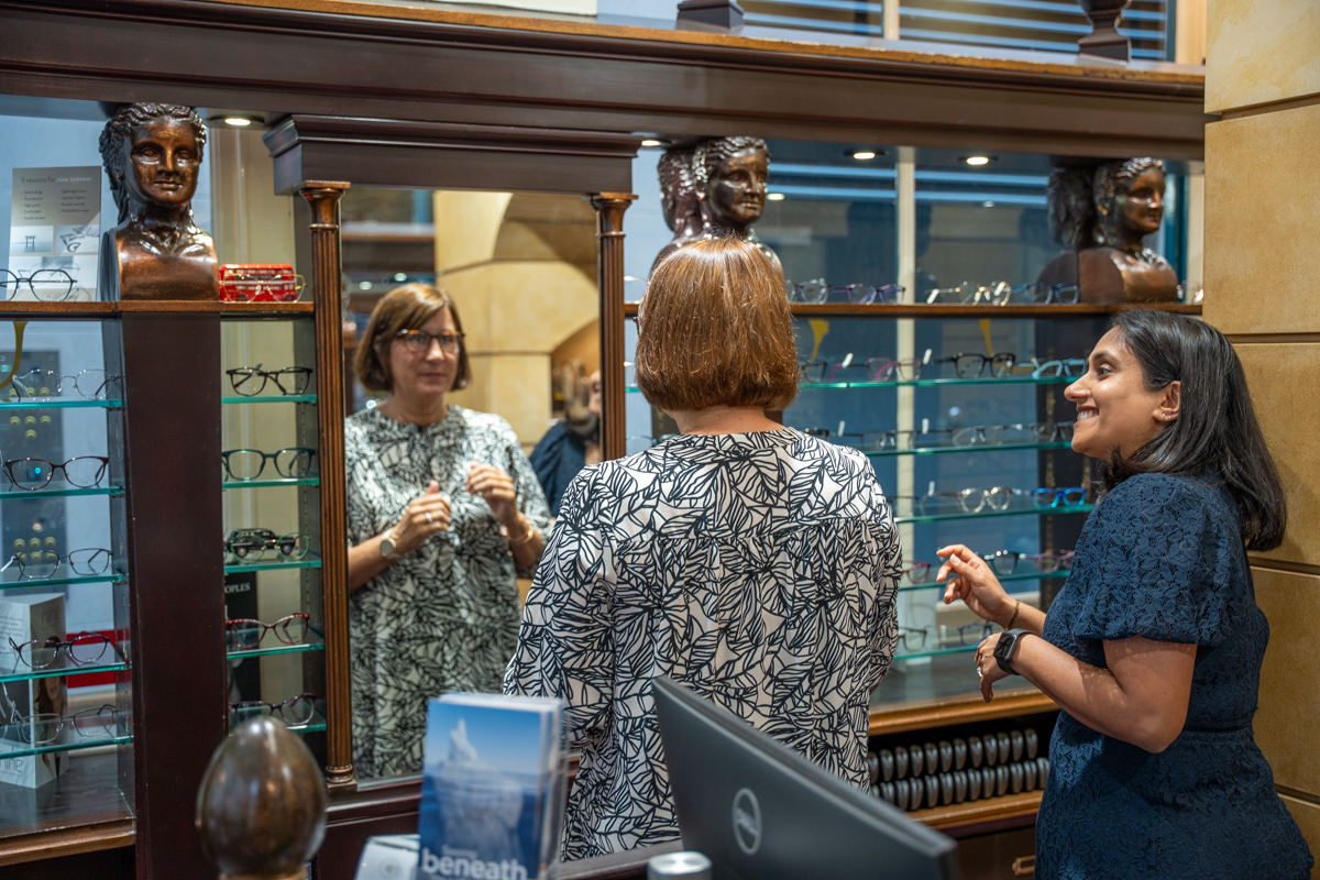 Optical store interior with display cases, eyeglasses, and people conversing