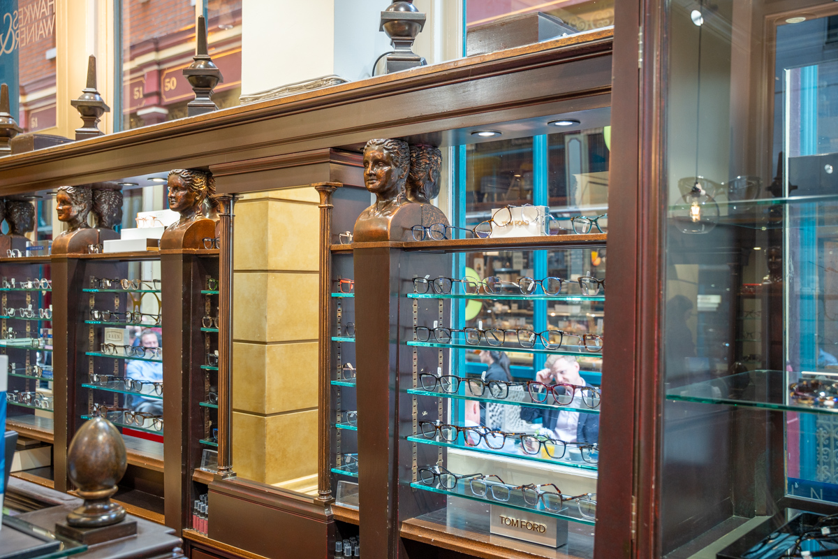 Vintage eyewear display with bronze busts and glass shelves of designer glasses