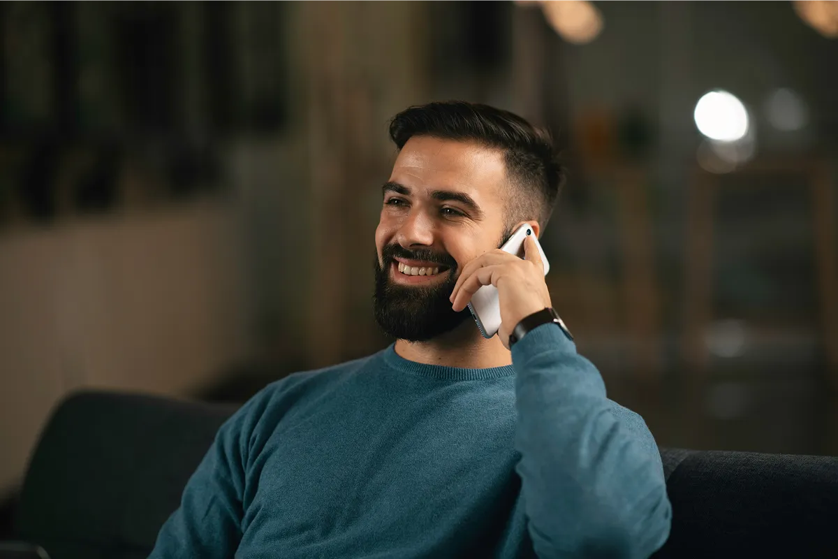 Image of a man smiling while talking on the phone in a modern, relaxed workspace, representing a confident and professional business environment.