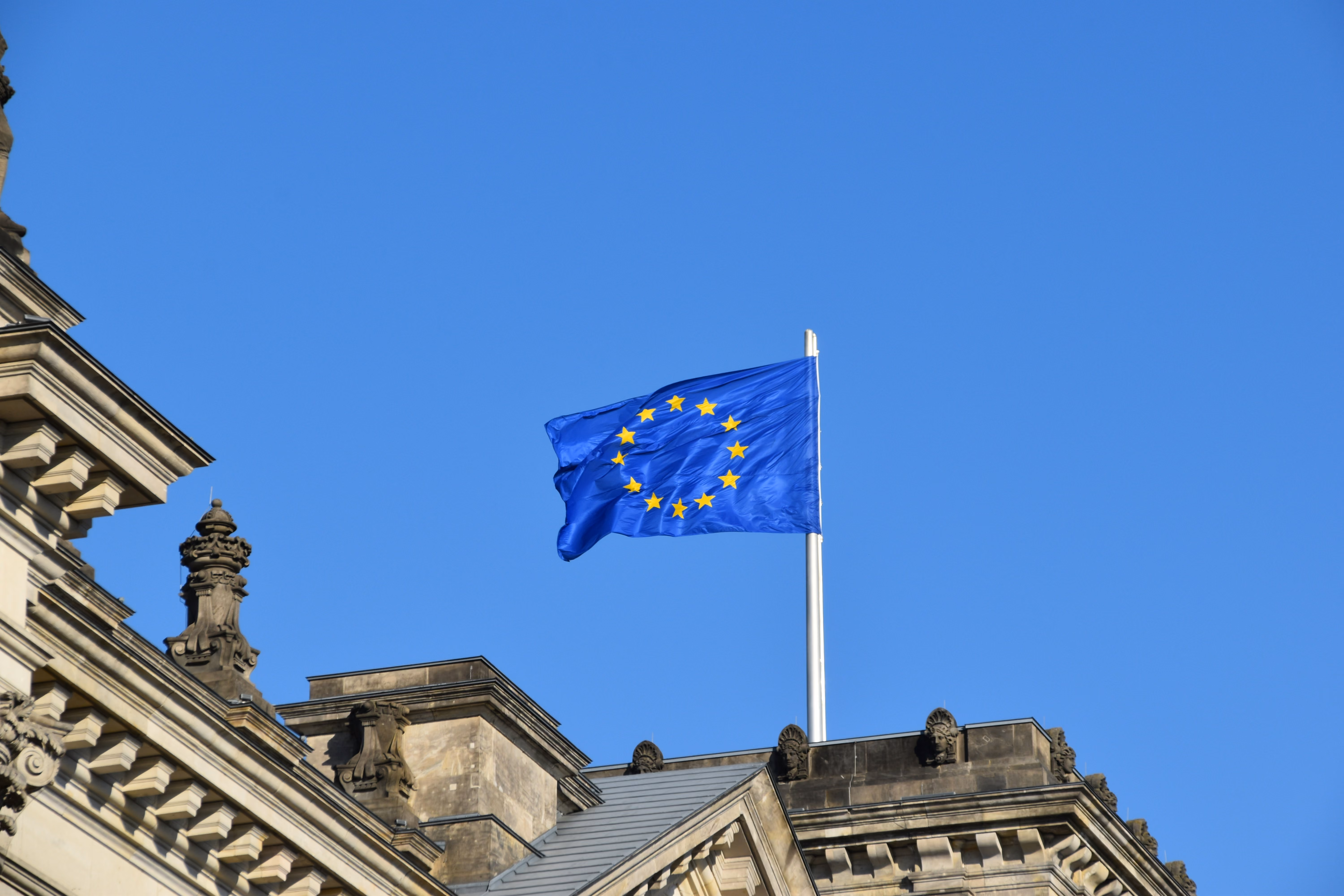 Drapeau européen flottant sur un bâtiment historique sous un ciel bleu clair.