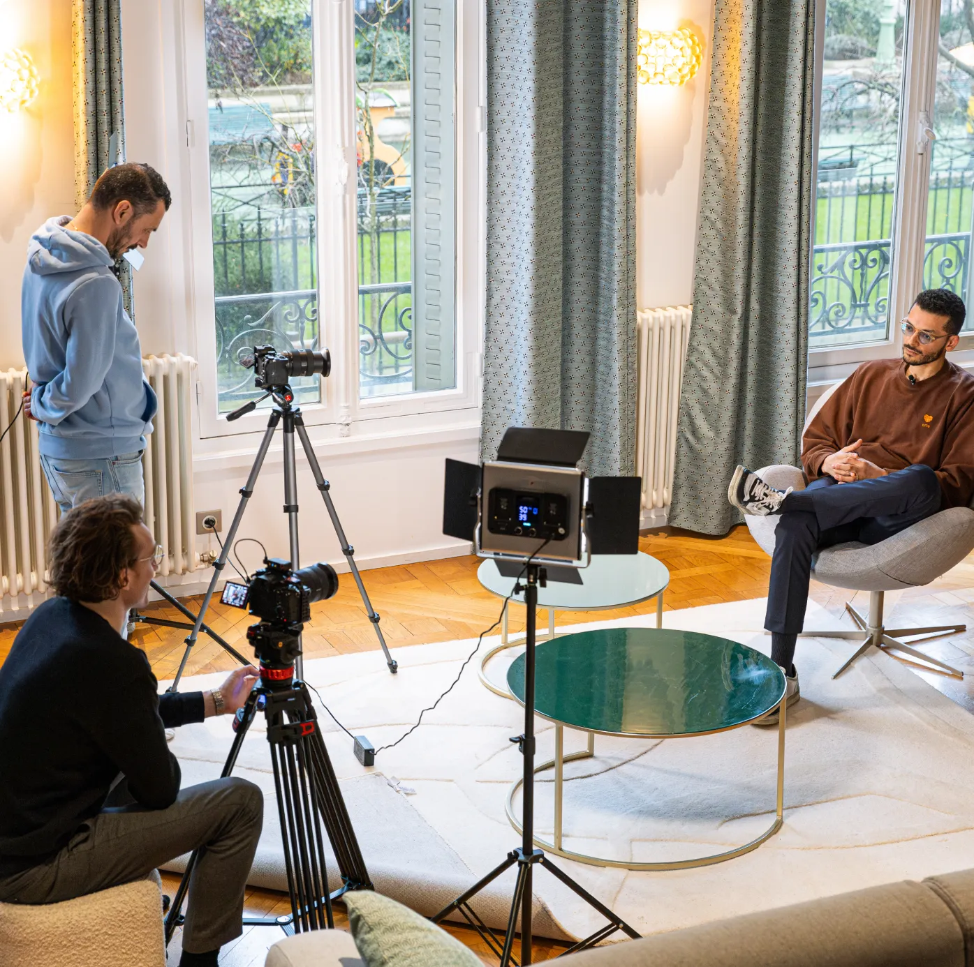  Indoor video shoot with a production team interviewing a seated guest, featuring professional lighting and camera setup.