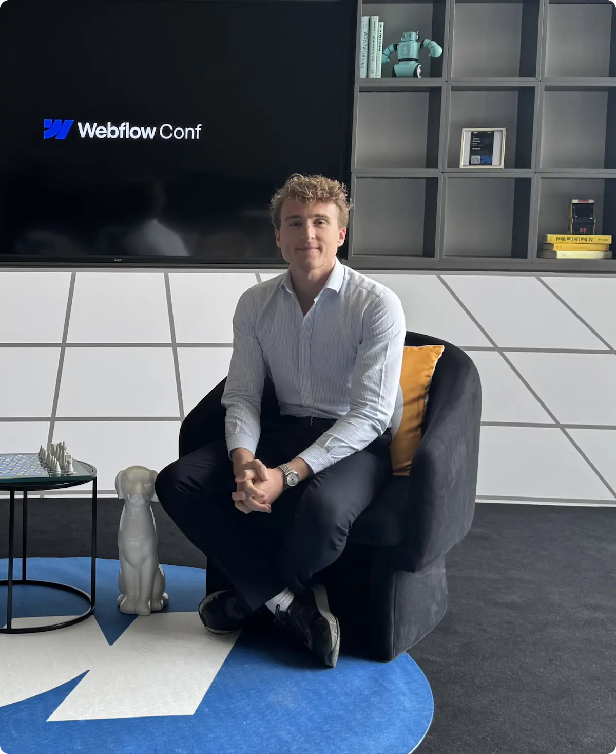 Florian Bodelot sitting in a black chair at Webflow Conf, with the event logo displayed on the screen behind him.