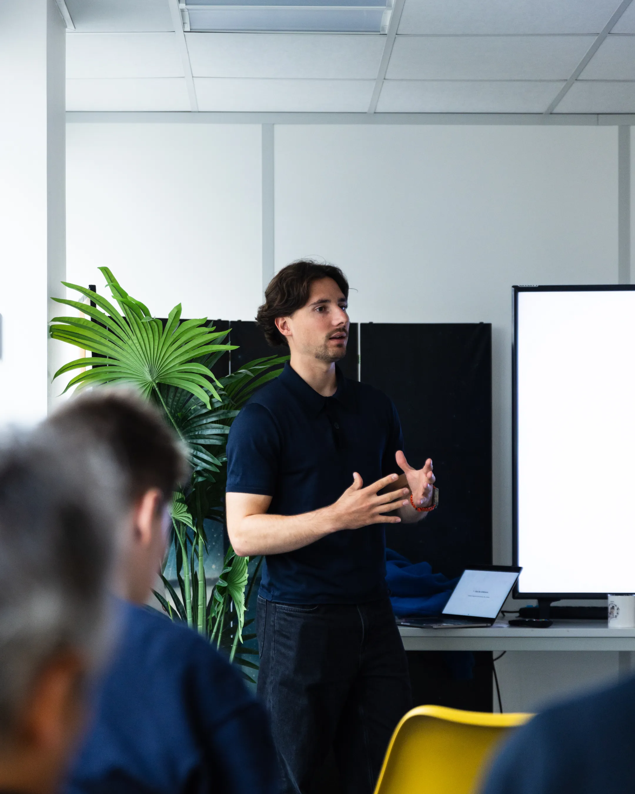 Personne donnant une présentation devant un petit groupe dans une salle de réunion, avec un écran en arrière-plan.