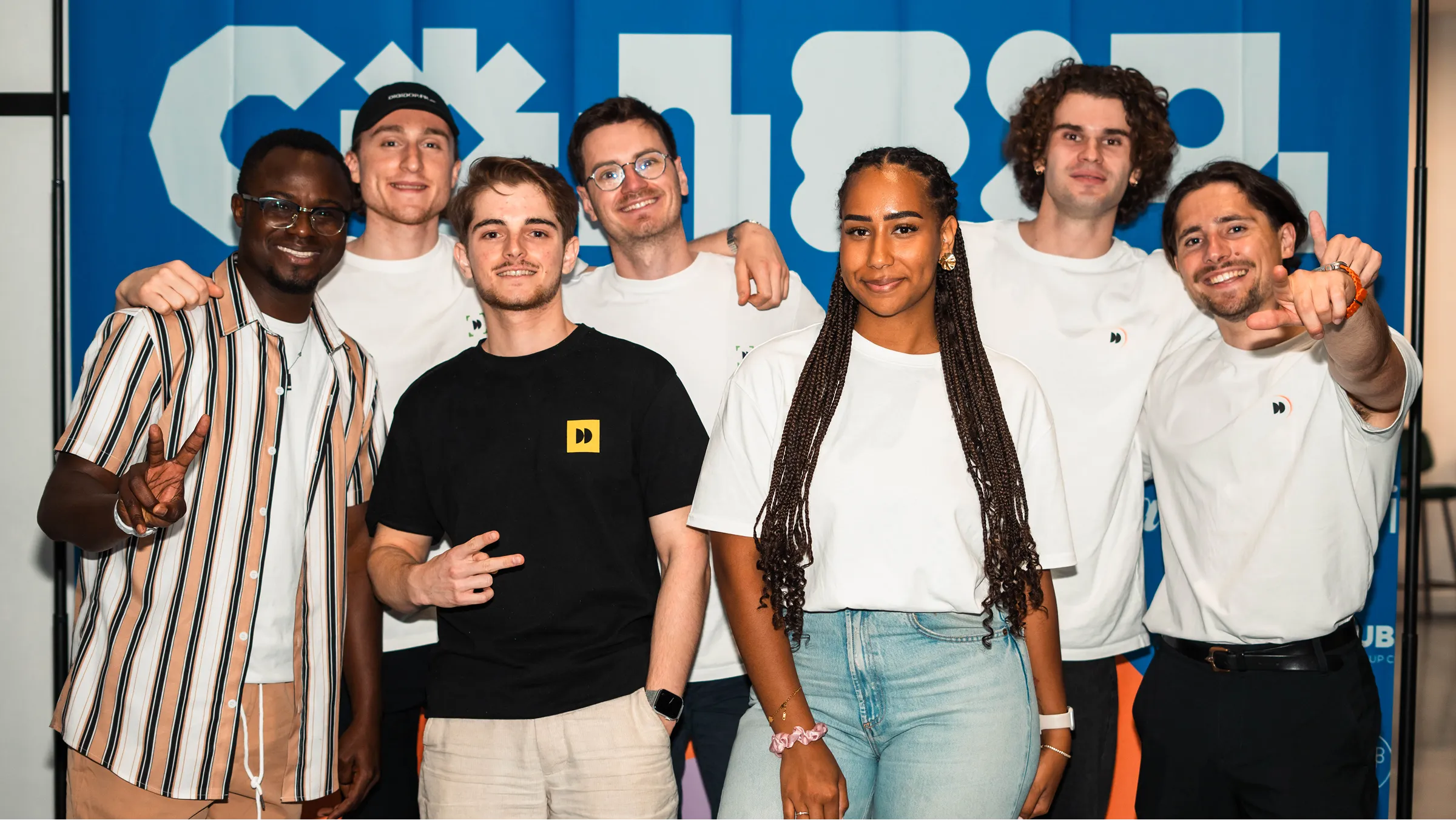 Group of smiling young adults posing together at an event, standing in front of a blue graphic backdrop.