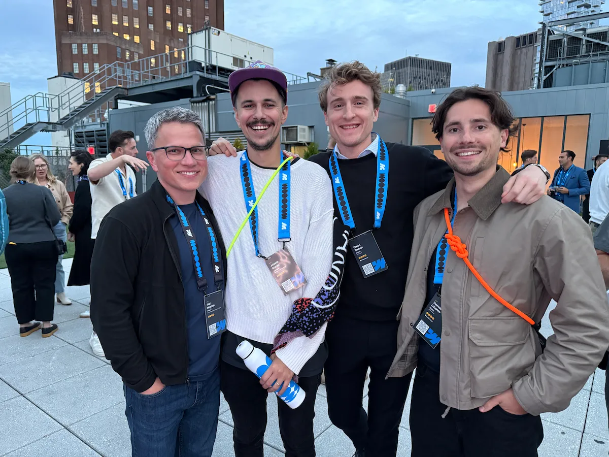 Four smiling people posing on a rooftop during an event, with buildings visible in the background.