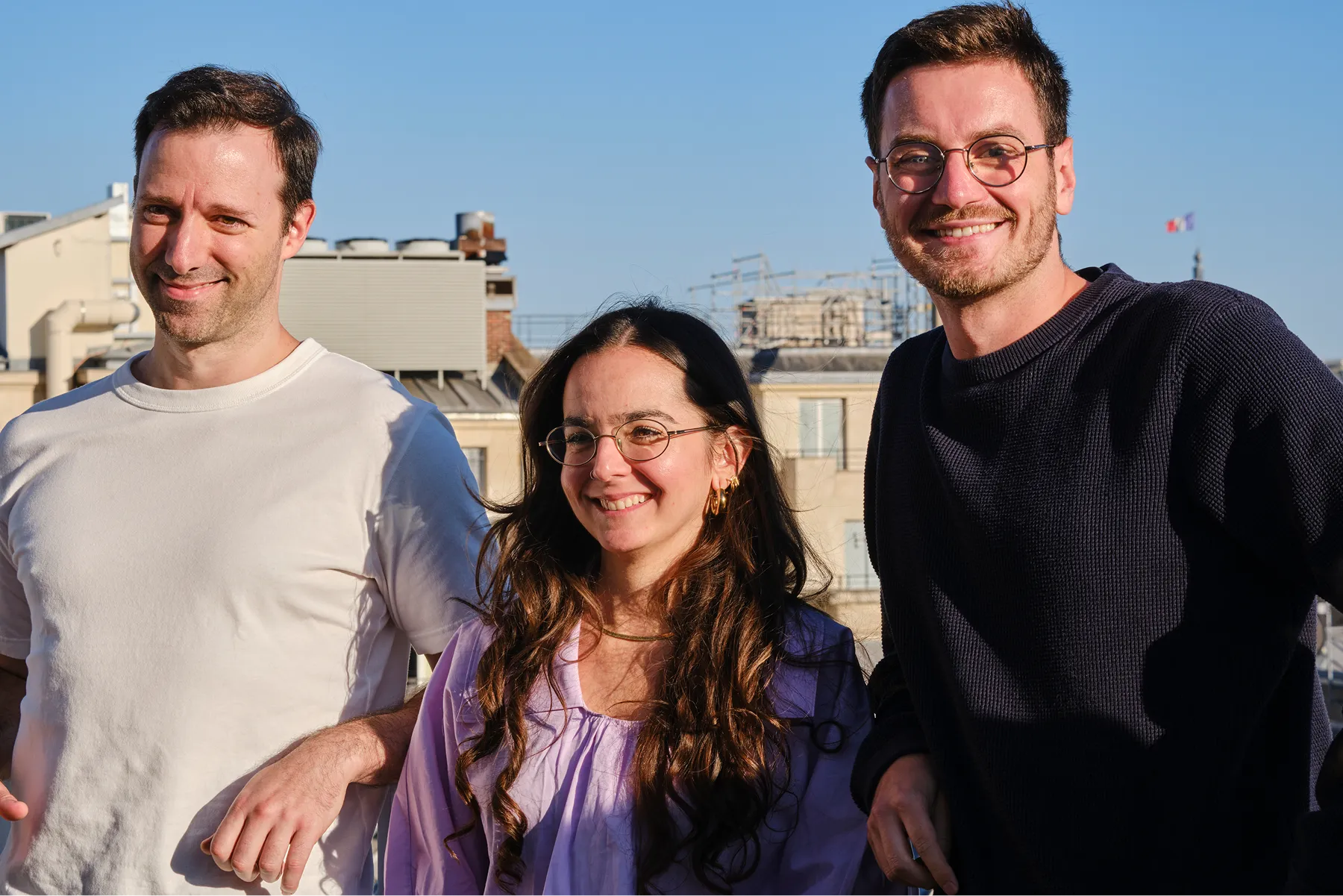 Portrait de trois membres d’équipe souriants sur un rooftop ensoleillé.
