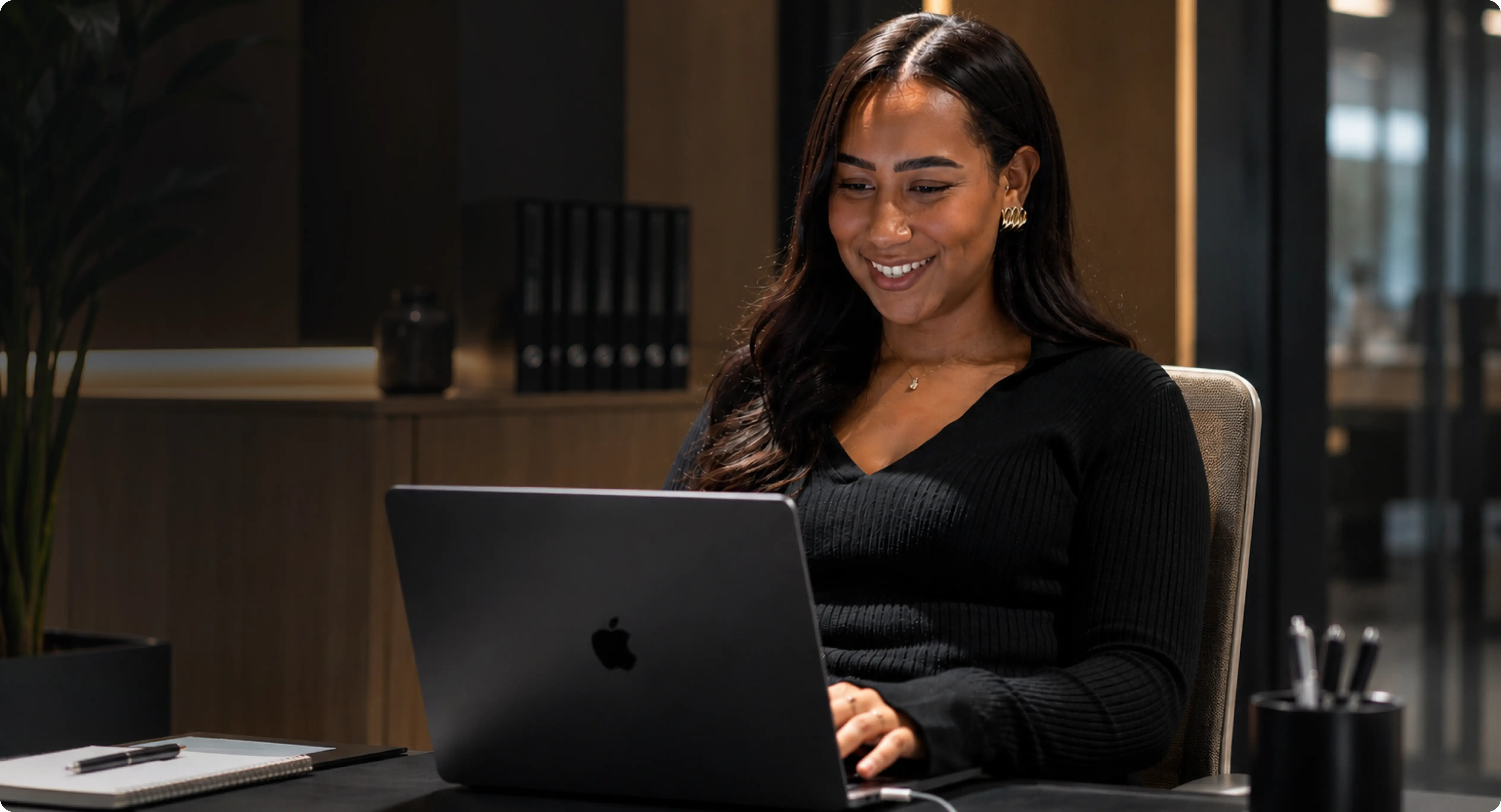 Océane, Project Manager chez Digidop, travaille sur son MacBook dans une salle de réunion moderne. Assise à une table dans un environnement de bureau premium, elle sourit en consultant son ordinateur, illustrant la gestion de projets web et la collaboration avec les équipes.