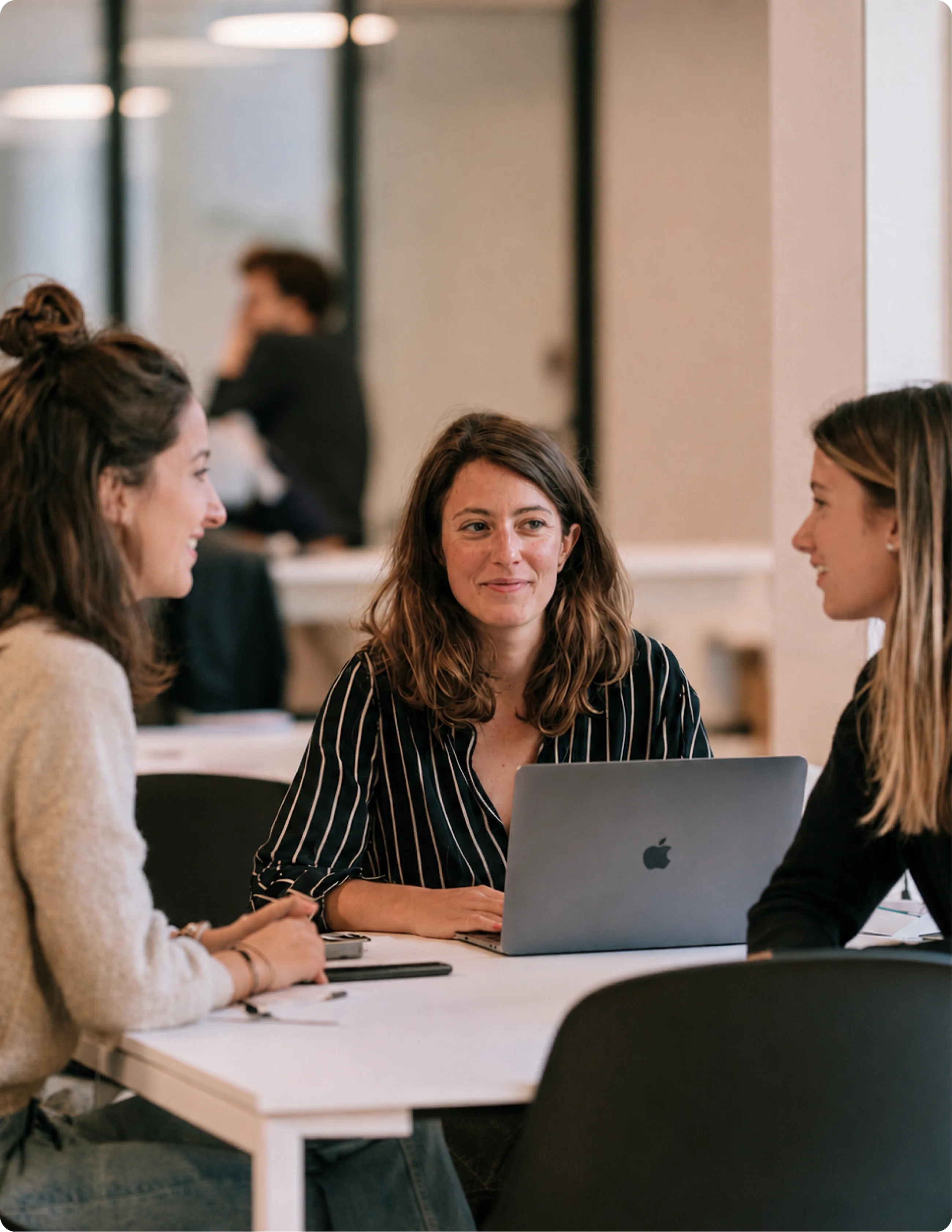 Trois femmes ont engagé une conversation autour d'une table avec un ordinateur portable dans un cadre de bureau moderne.