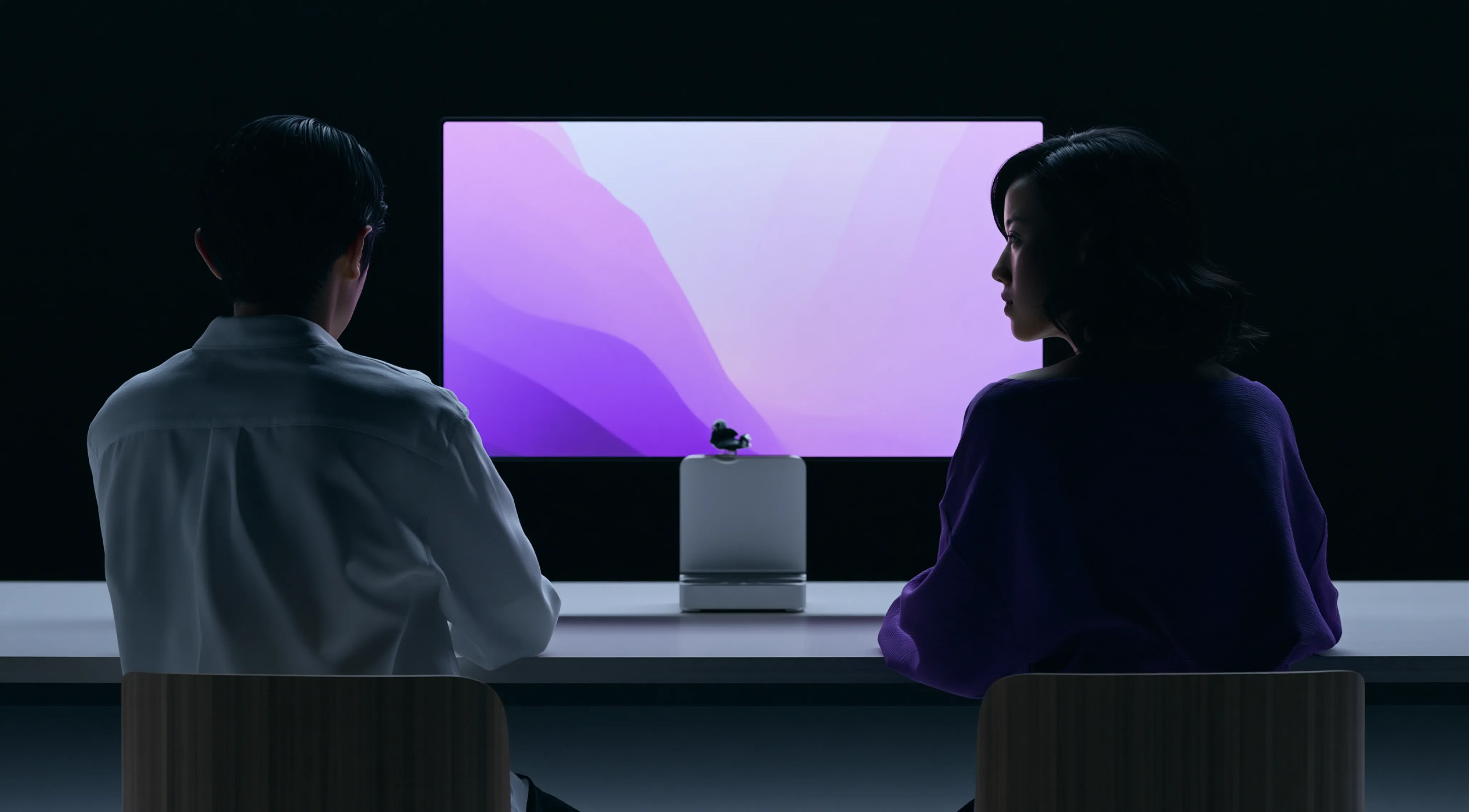 Vue arrière de deux personnes assises à une table face à un grand écran avec des visuels abstraits violets.