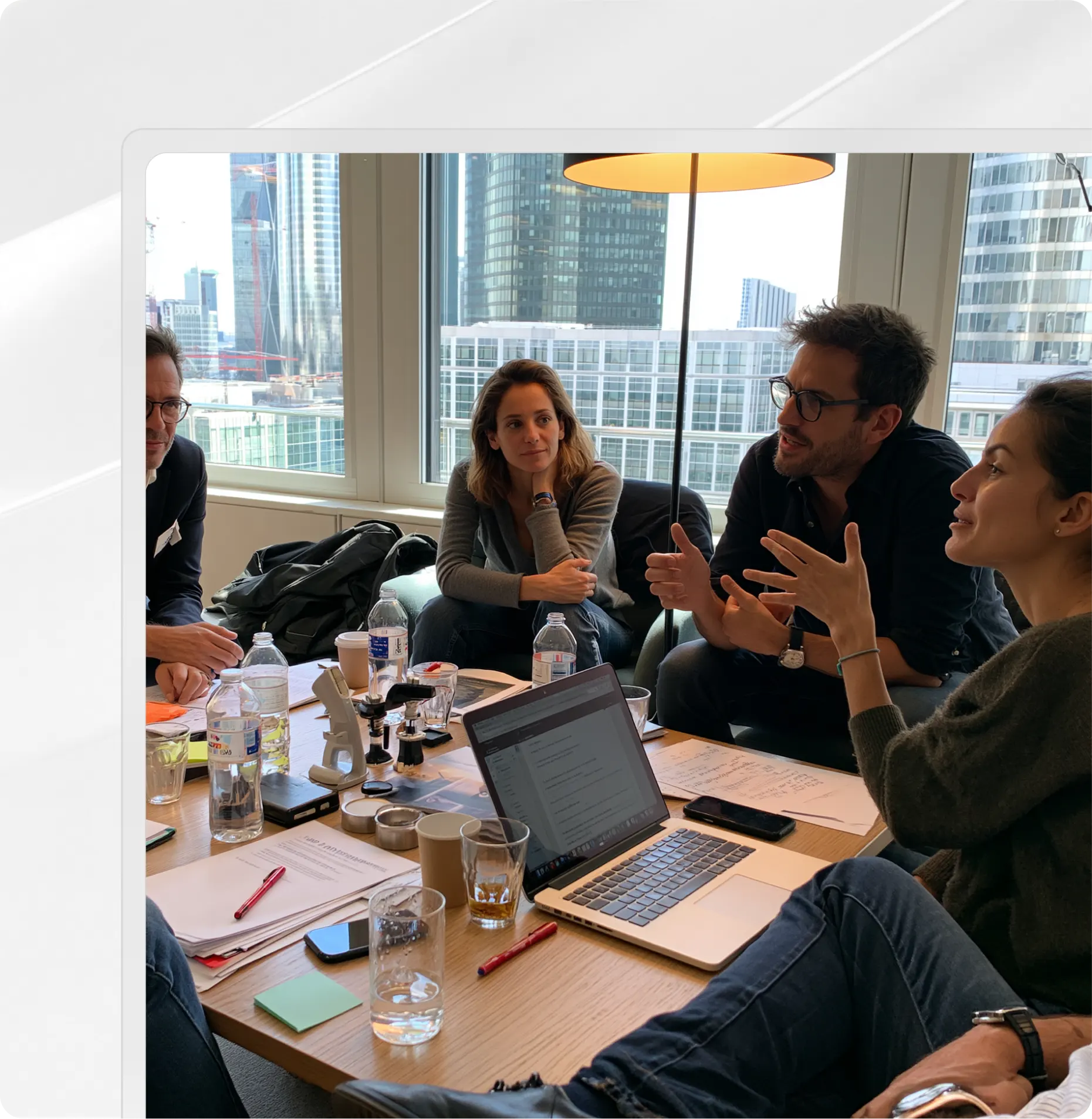 Quatre personnes ont participé à une discussion autour d'une table avec des ordinateurs portables, des papiers et des bouteilles d'eau dans un bureau.