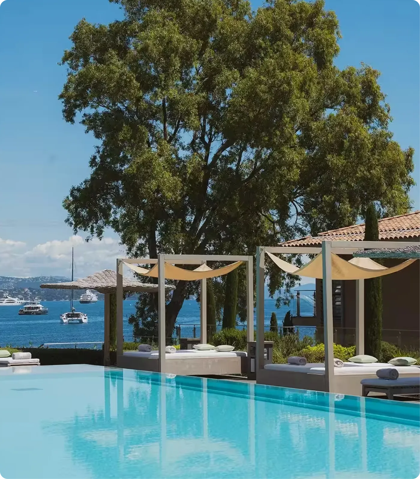 Outdoor swimming pool with lounge areas overlooking the sea, surrounded by greenery.