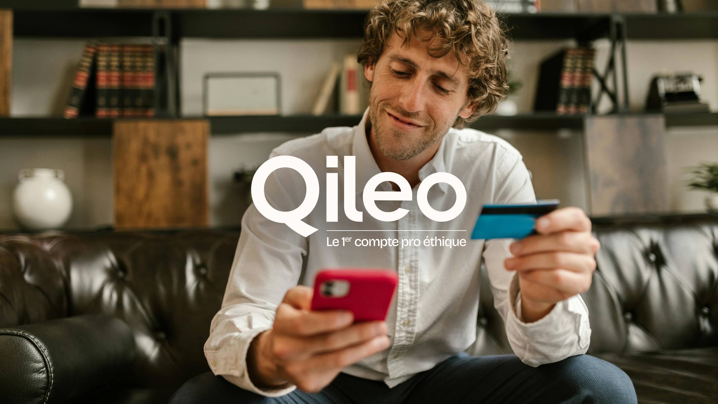 Photo d'un entrepreneur qui est assit il tient une carte bancaire et regarde son application bancaire sur son téléphone