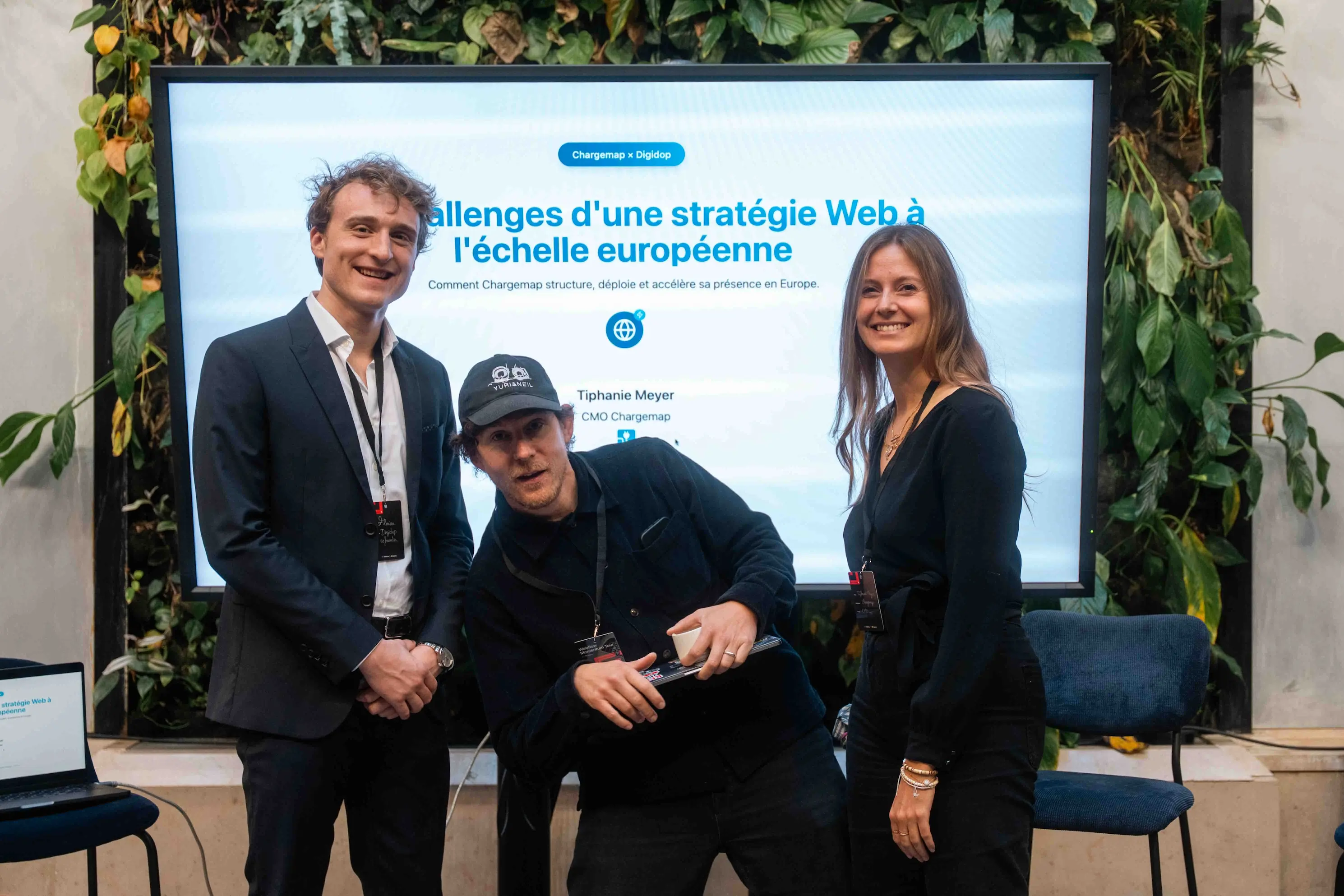 Three speakers smiling in front of a screen displaying the talk “Challenges of a Web Strategy at the European Scale” during the Webflow Momentum Tour Paris.