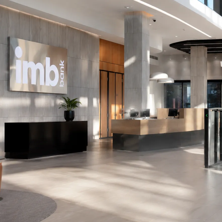 Espace d’accueil contemporain d’IMB Bank avec un vaste hall baigné de lumière naturelle, des finitions haut de gamme, des comptoirs d’accueil modernes et une architecture chaleureuse reflétant la confiance et le professionnalisme.