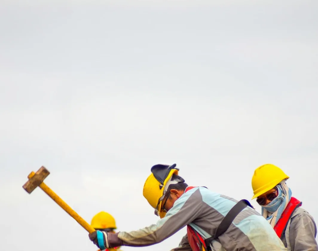 Construction workers wearing yellow safety helmets working with a sledgehammer.