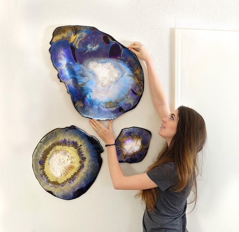 A person hanging three geode-shaped wall panels finished in blue and gold resin.