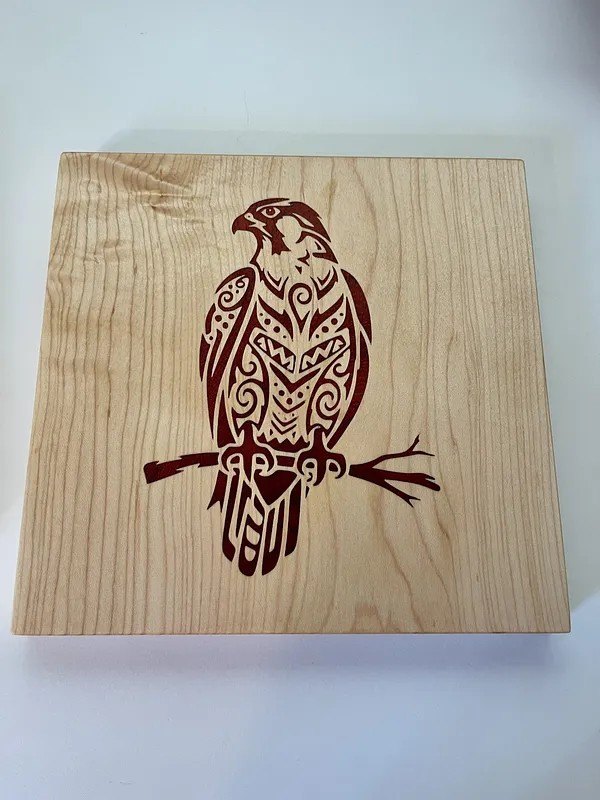 An eagle inlaid in dark padauk into a pale maple panel, cut as a V-carve inlay.