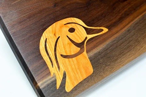 A duck head inlaid in pale wood into a dark live-edge board.