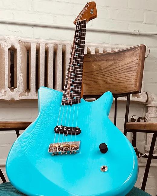 A blue solid body electric guitar with a maple neck, leaning against a chair.