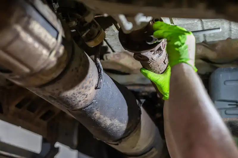 Driveshaft removal underway; technician in neon gloves loosens rusted flange under chassis for heavy-duty truck