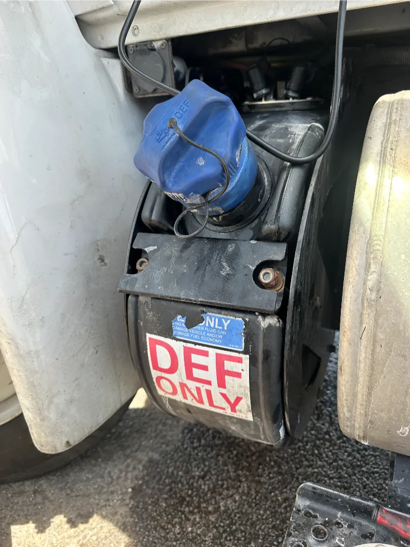 Heavy-duty truck repair service showing DEF tank with blue cap and DEF ONLY label mounted behind cab near fuel system.