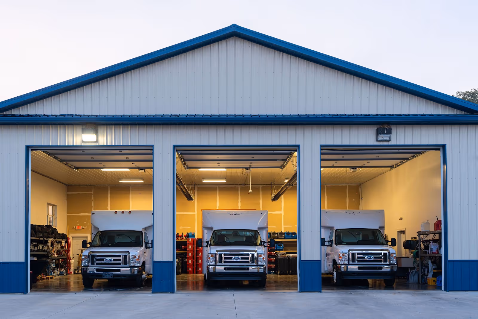 Three work trucks each sit within a bay of a blue and white three car garage.