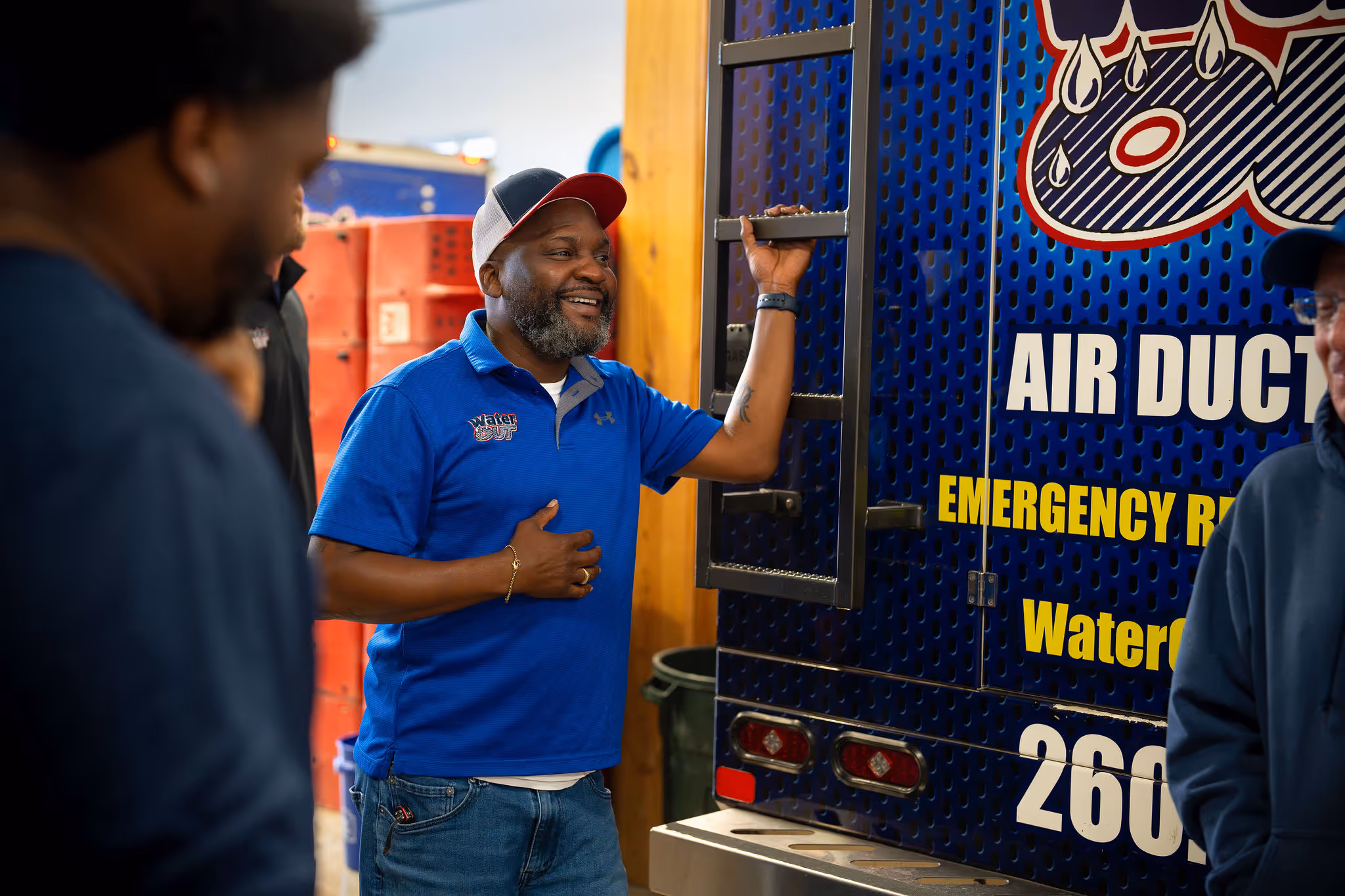 A person laughs with two other people while holding the ladder of a Water Out service truck.