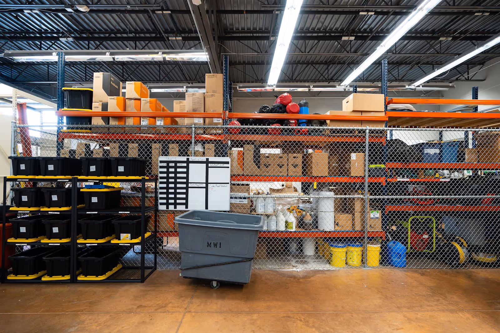 A warehouse with stacked bins, boxes, and a rolling trash bin
