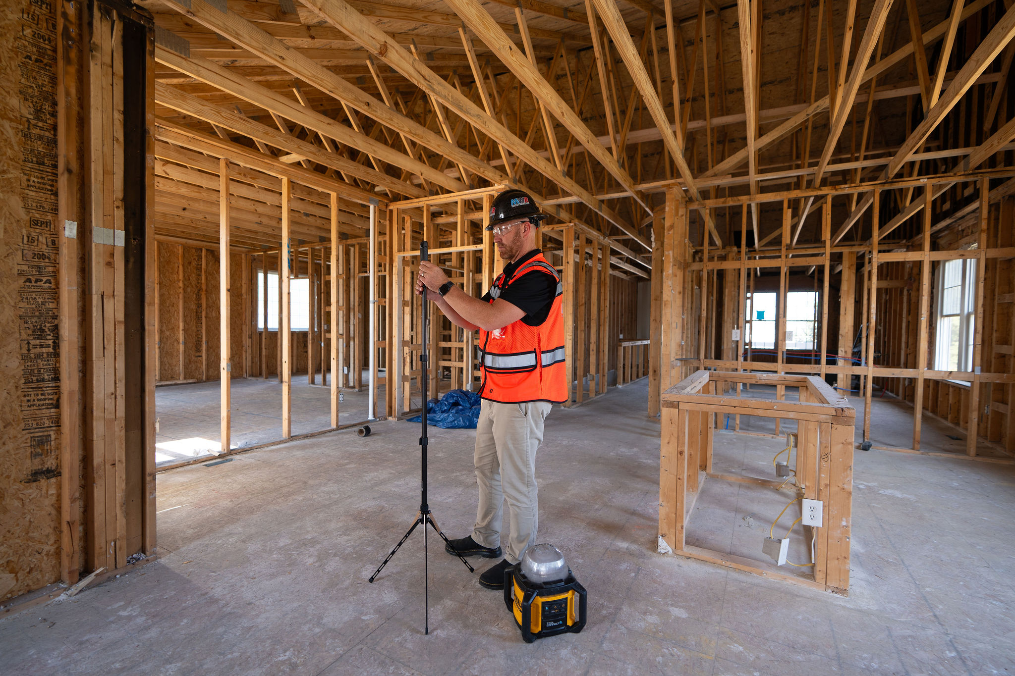 A person wearing a hard hat and orange vest takes a 360˚ capture of a construction site that's down to the studs.