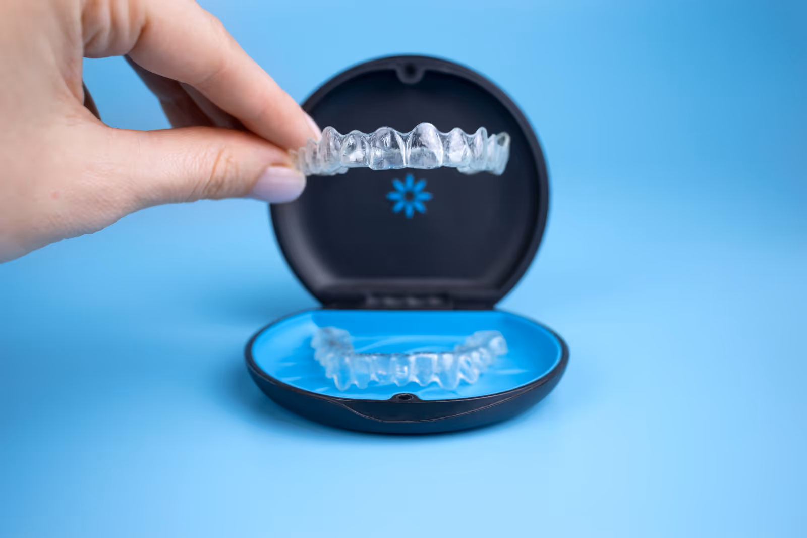 Woman holding invisalign transparent retainers with a box on the table, flatlay top view
