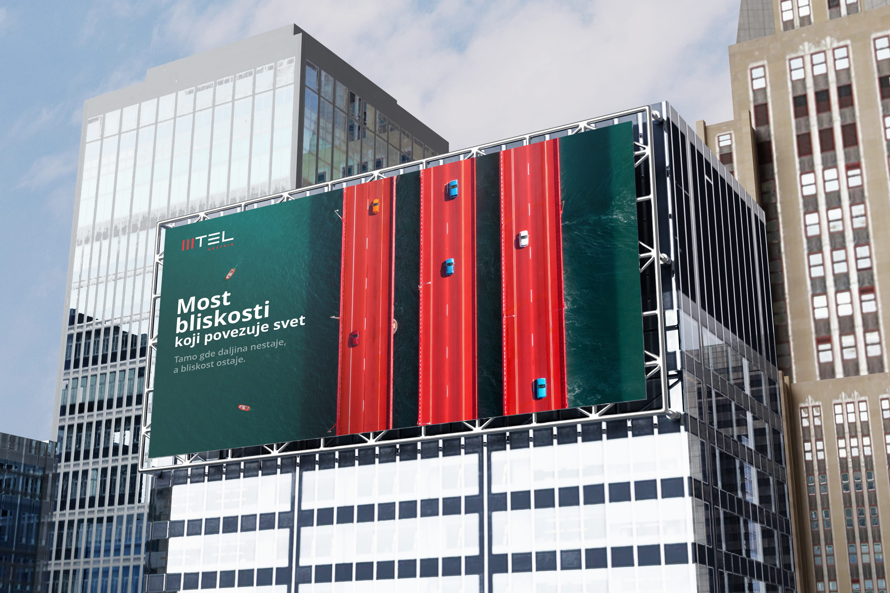 Billboard on city building with aerial view of red bridge and cars over blue water.
