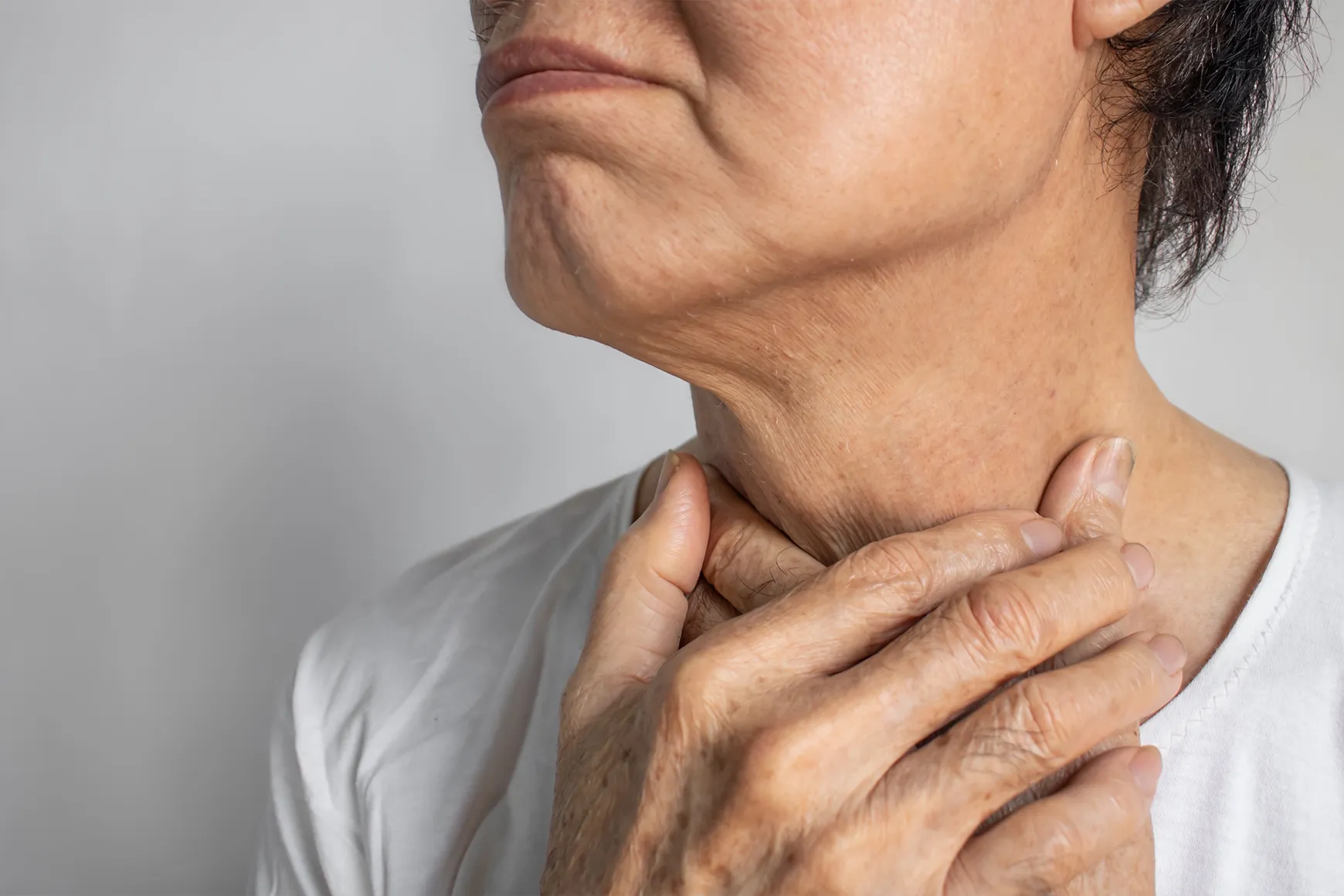 A close-up of an older person holding their throat with both hands, appearing to have difficulty swallowing