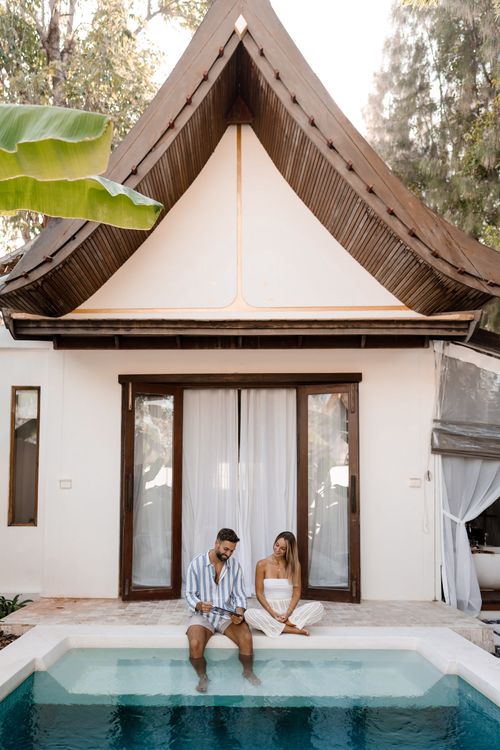A man and a woman sitting on the edge of a pool.