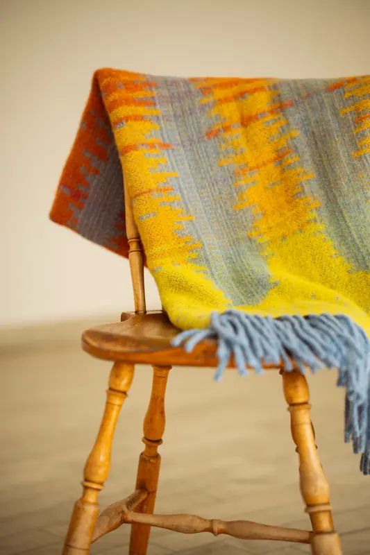 Vävd pläd i gult, orange och gråblått, draperad över en trästol.
