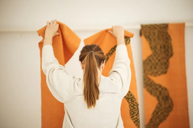 Orange väggtextilier med gröna mönster justeras vid upphängning.