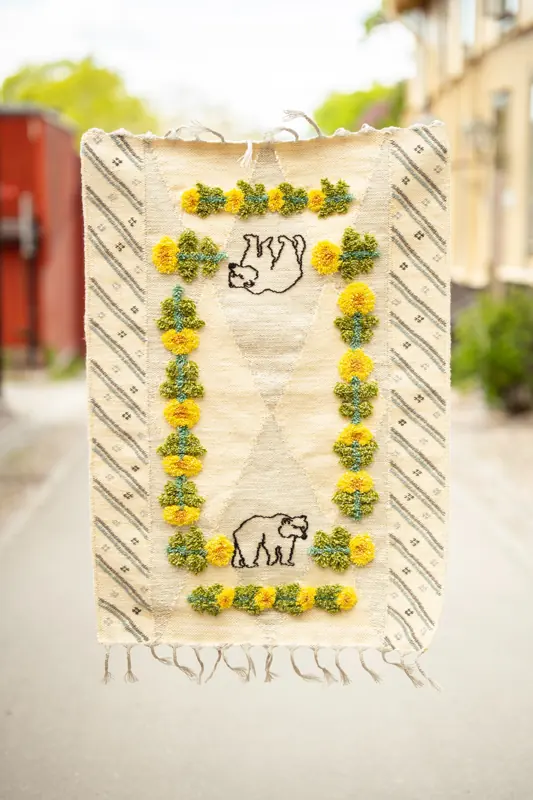 Ljus vävd textil med björnmotiv och gula och gröna blommor i relief.